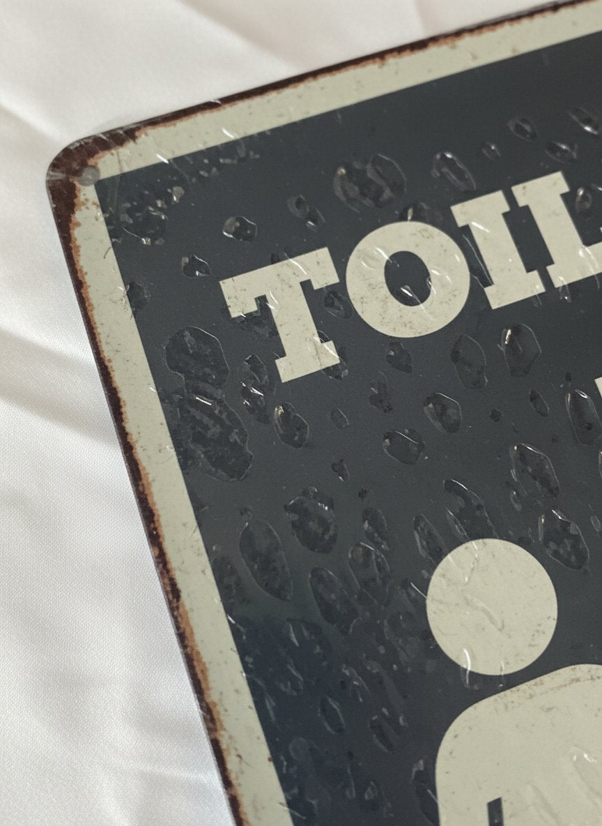 Placca toilet vintage in metallo nero con dettagli bianchi, design retrò con grafiche geometriche e bordi usurati