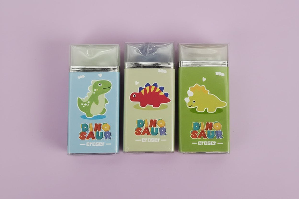 Tre gomme per cancellare a forma di dinosauro colorati in blu, beige e verde con dettagli gialli e rossi, packaging