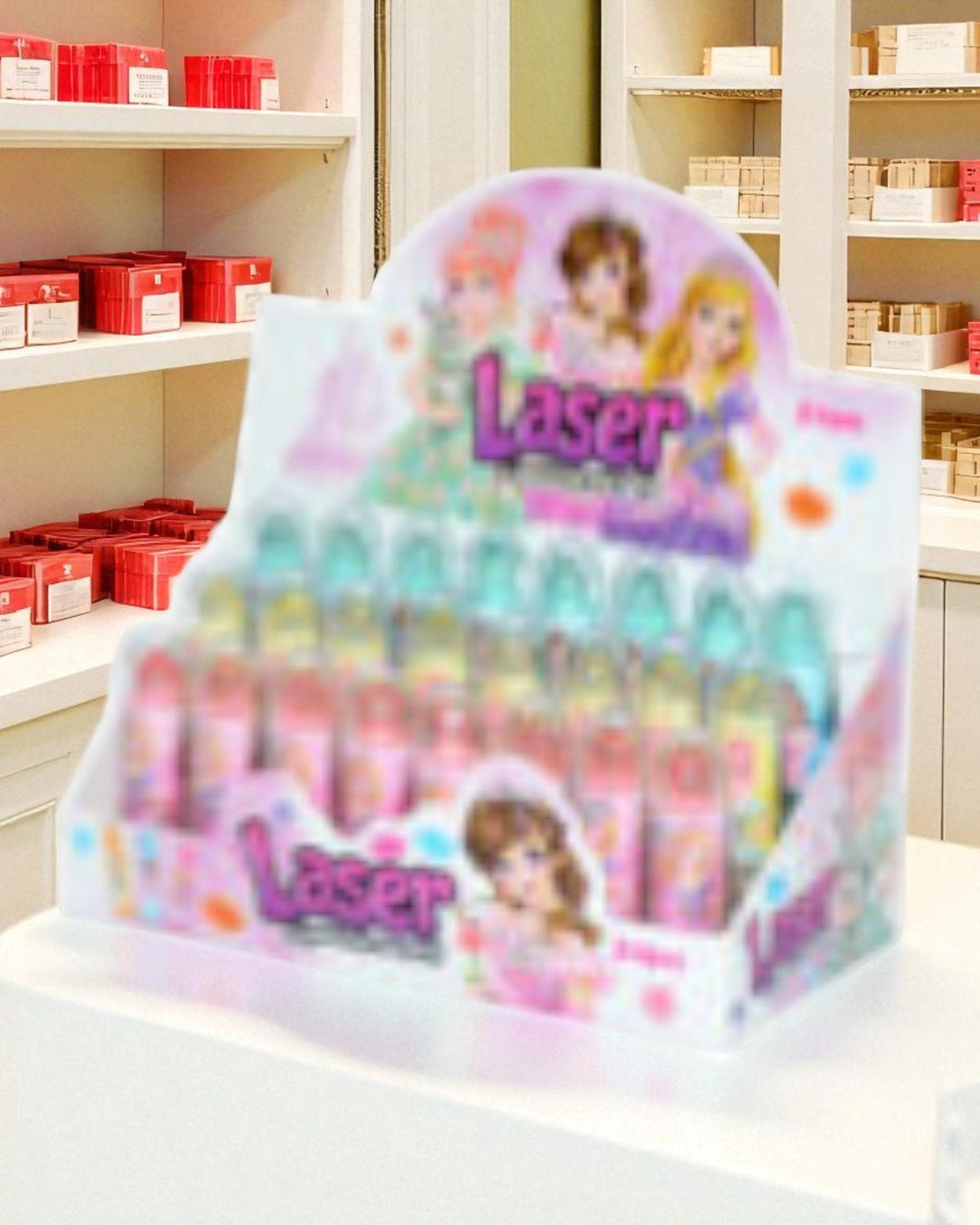 Lipstick Laser 5 gr display box con bambine colorate, packaging rosa e azzurro, scaffali farmacia sullo sfondo