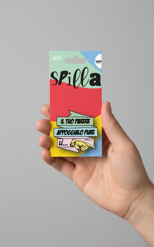 Spilla colorata con scritta "Il tuo parere appoggialo pure" su sfondo rosso, giallo e blu, tenuta in mano