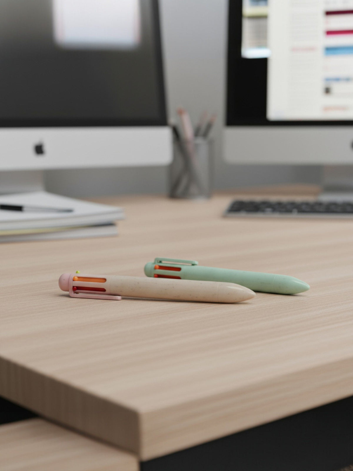 Penna multicolor pastello rosa e verde con punte colorate su scrivania in legno davanti a monitor e tastiera