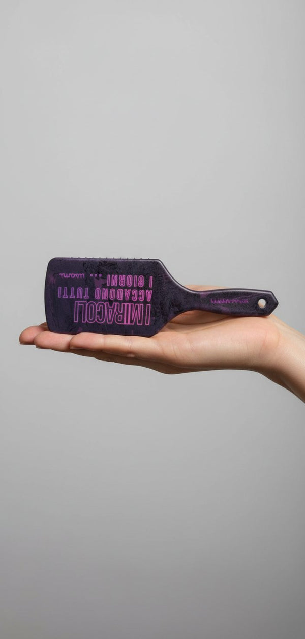 Spazzola per capelli nera con scritte in neon fucsia e manico decorato con fantasia pettini su sfondo rosa