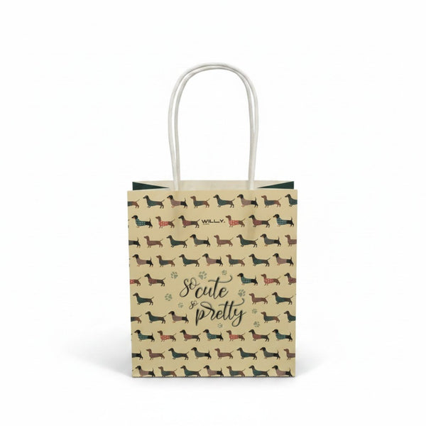 Shopper in carta kraft con pattern ripetuto di bassotti in diversi colori e fantasie, manici bianchi in cotone, scritta So Cu