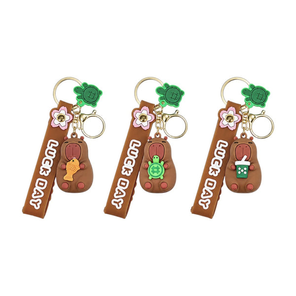 Tre portachiavi a forma di capibara marrone con fiori rosa, accessori verdi e anellino dorato, stile kawaii