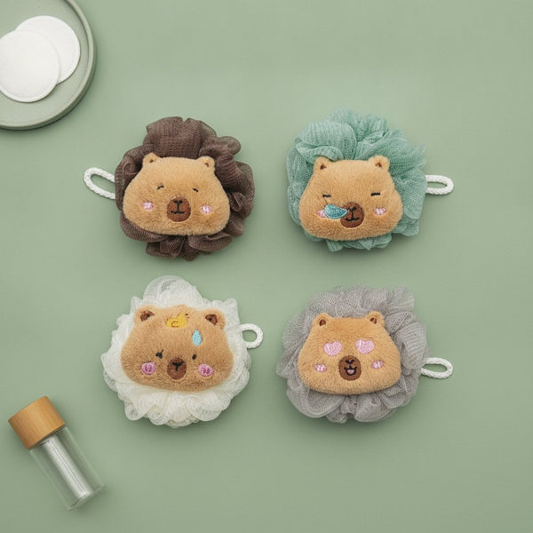 Quattro spugne da bagno a forma di capibara con testa in peluche beige e corona in tulle nei colori marrone, verde acqua, bia