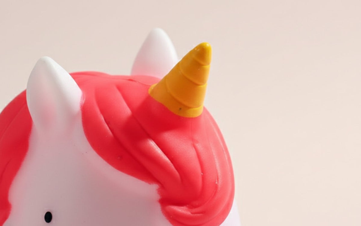 Lampada unicorno rosa e bianca con corno dorato e dettagli morbidi su sfondo beige