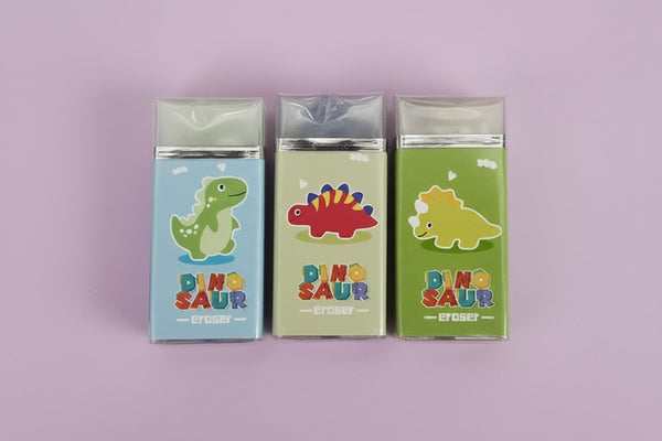 Tre gomme per cancellare a forma di dinosauro colorati in blu, beige e verde con dettagli gialli e rossi, packaging